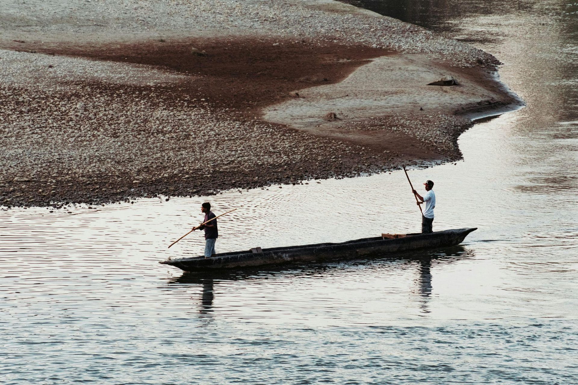 Boatmen guiding a dugout canoe past a sandbank on the river